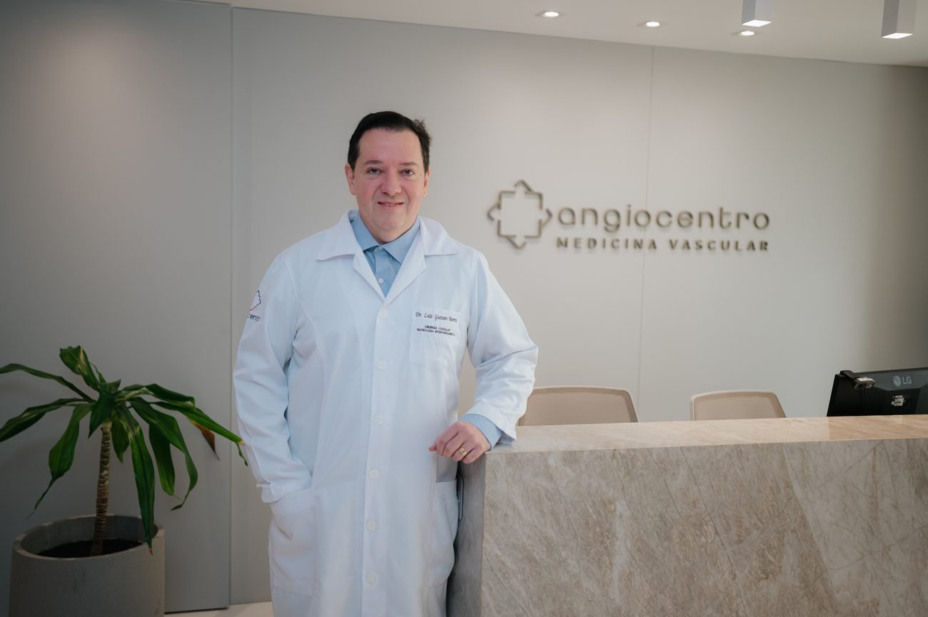 Médico da Angiocentro na recepção da clínica, com a marca Angiocentro Medicina Vascular na parede